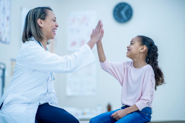 Young girl in pink shirt high fives female doctor in white coat